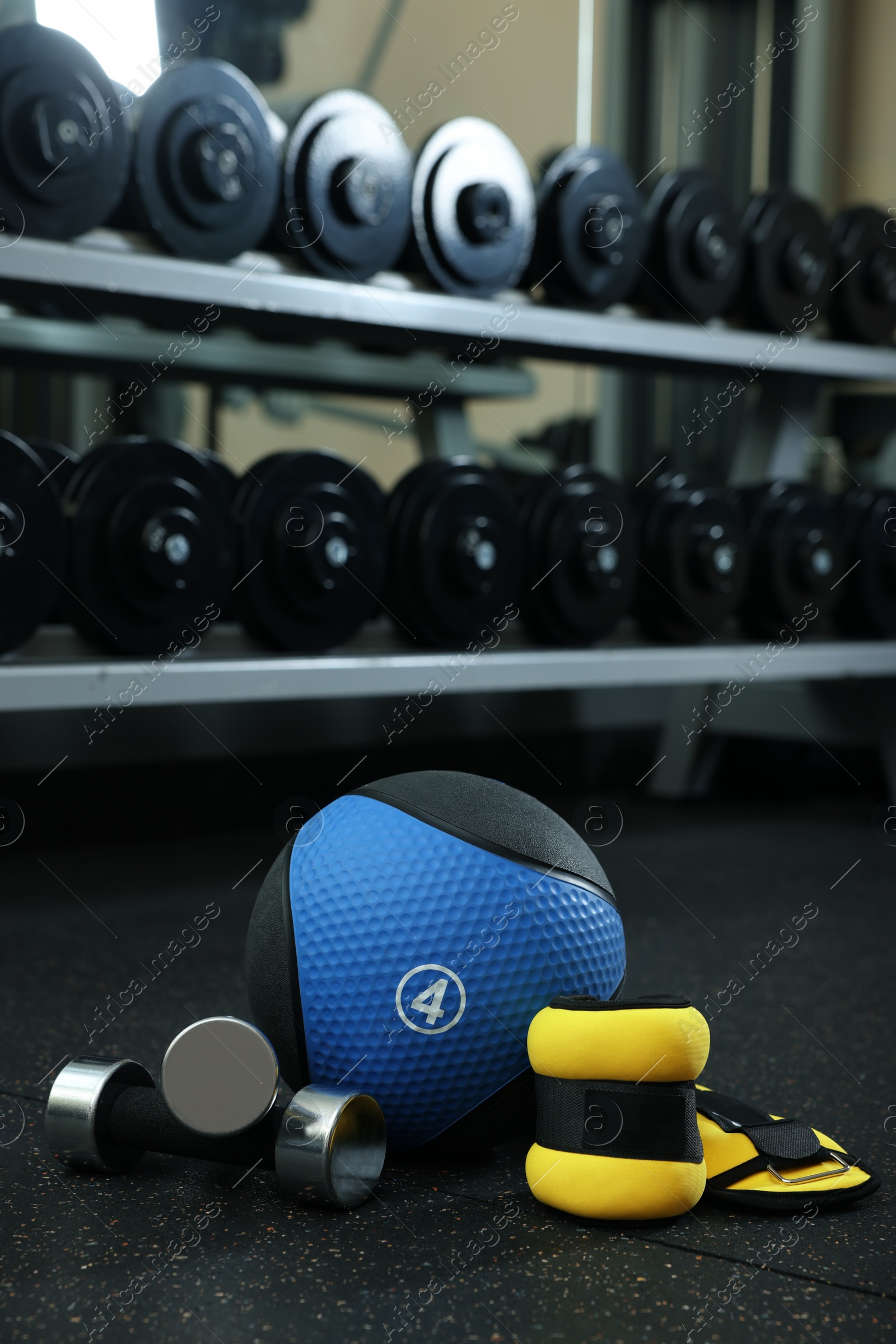 Photo of Blue medicine ball, weighting agents and dumbbells on floor in gym, space for text