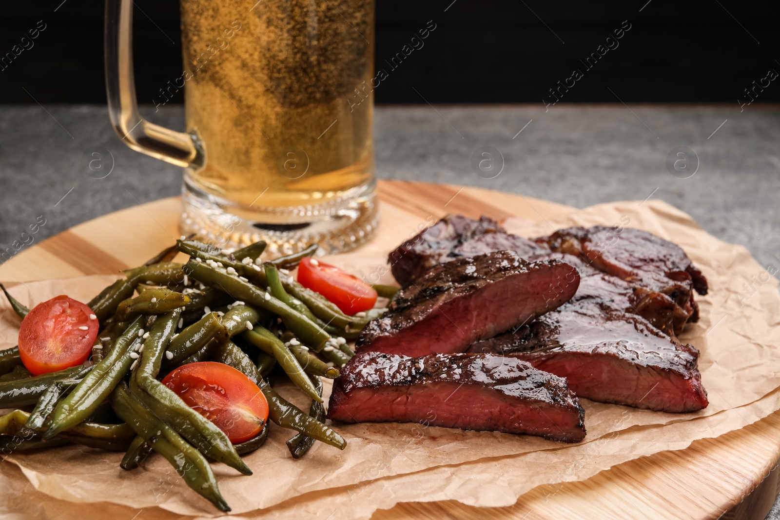 Photo of Mug with beer, delicious fried steak and asparagus on grey table