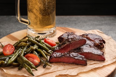 Mug with beer, delicious fried steak and asparagus on grey table