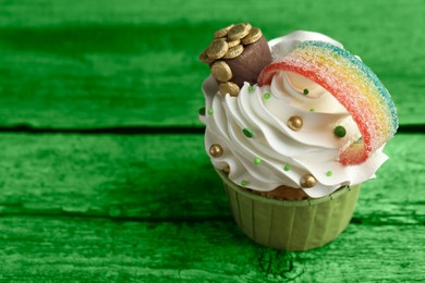 Image of St. Patrick's day. Tasty cupcake with sour rainbow belt and pot of gold toppers on green wooden table, closeup. Space for text