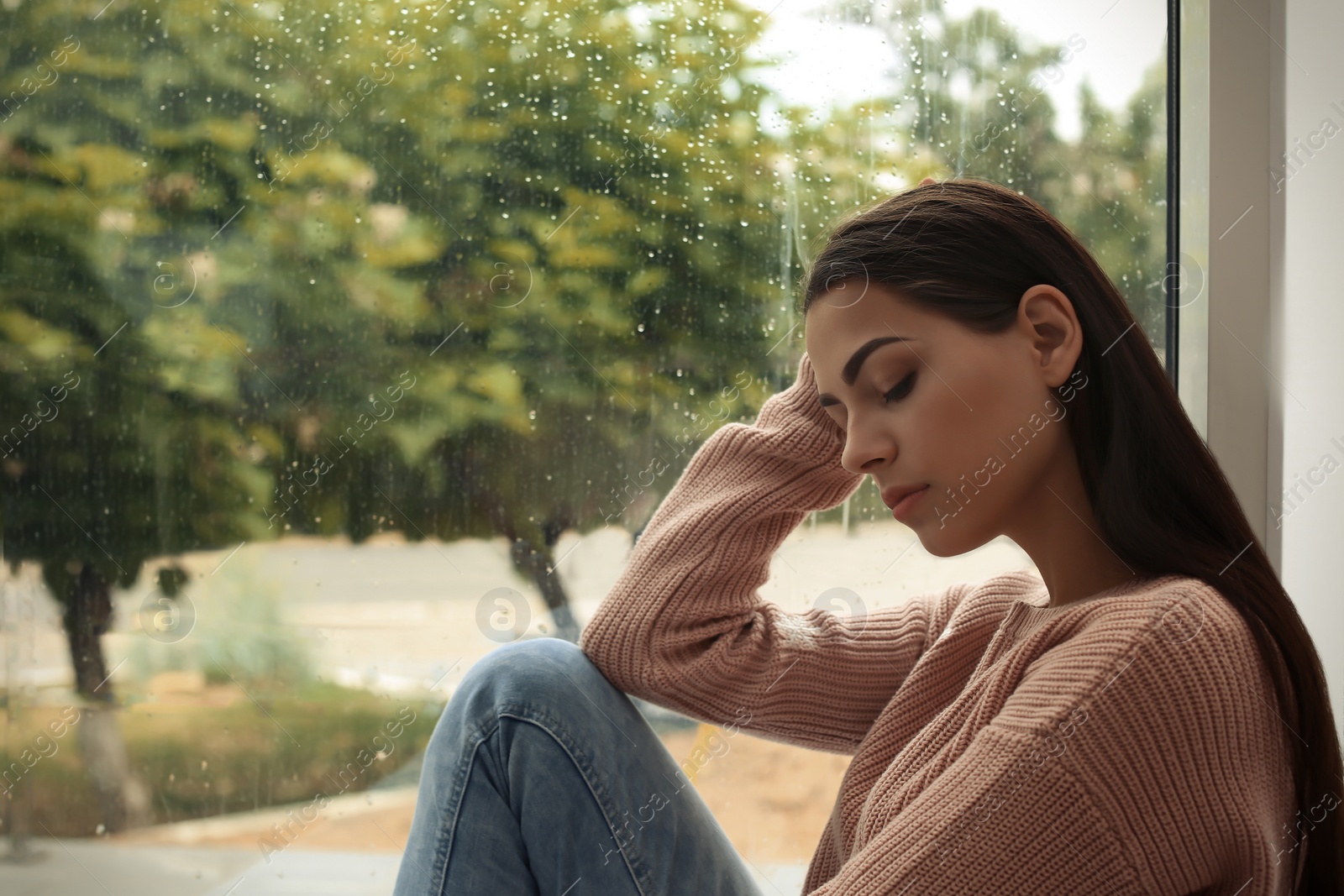 Photo of Young sad woman sitting near window at home