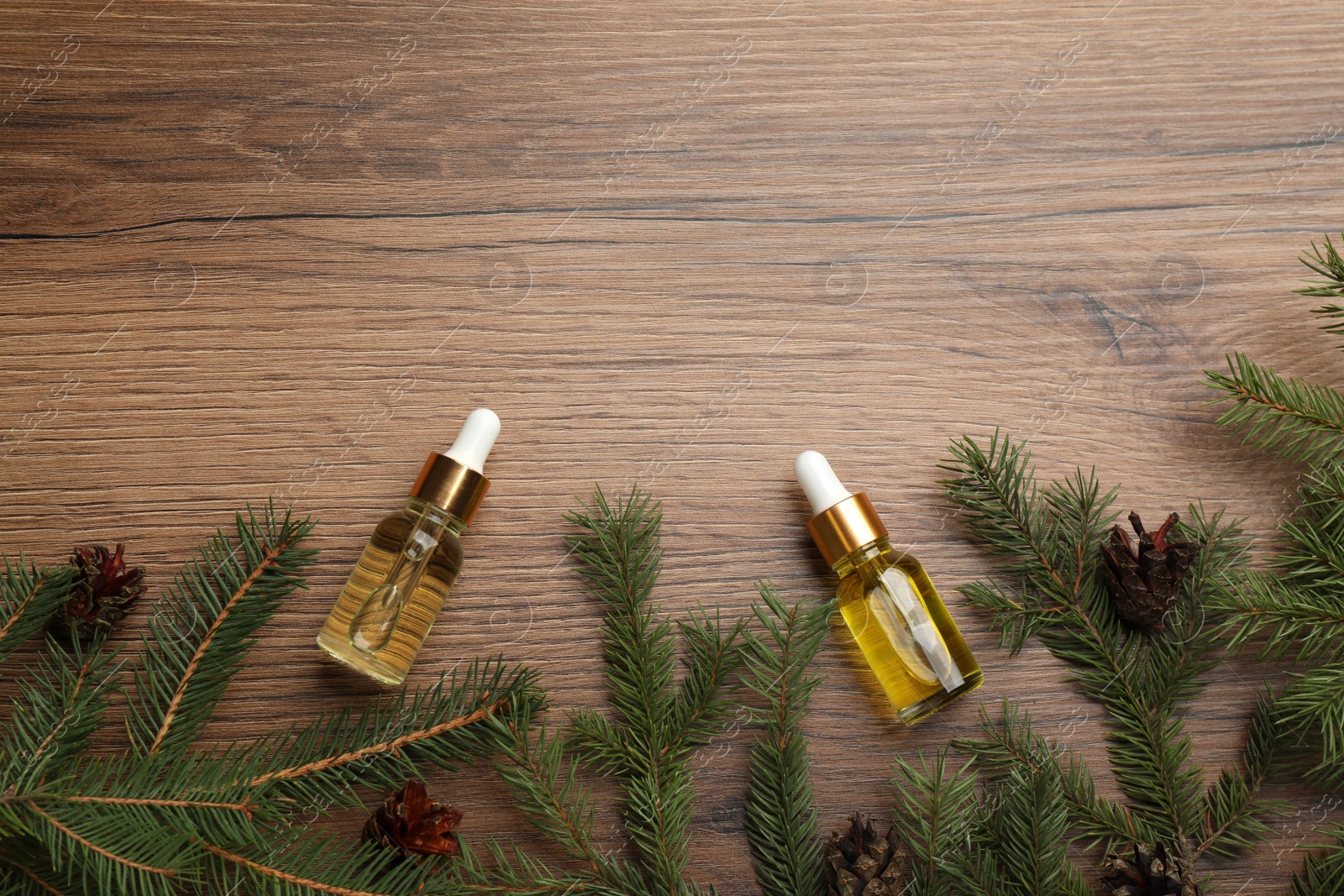 Photo of Pine essential oil, cones and branches on wooden table, flat lay. Space for text