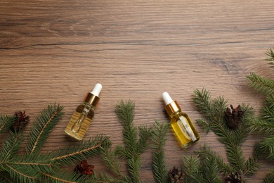 Pine essential oil, cones and branches on wooden table, flat lay. Space for text