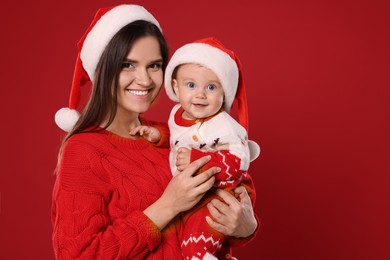 Photo of Happy mother with cute baby in Christmas outfits and Santa hats on red background