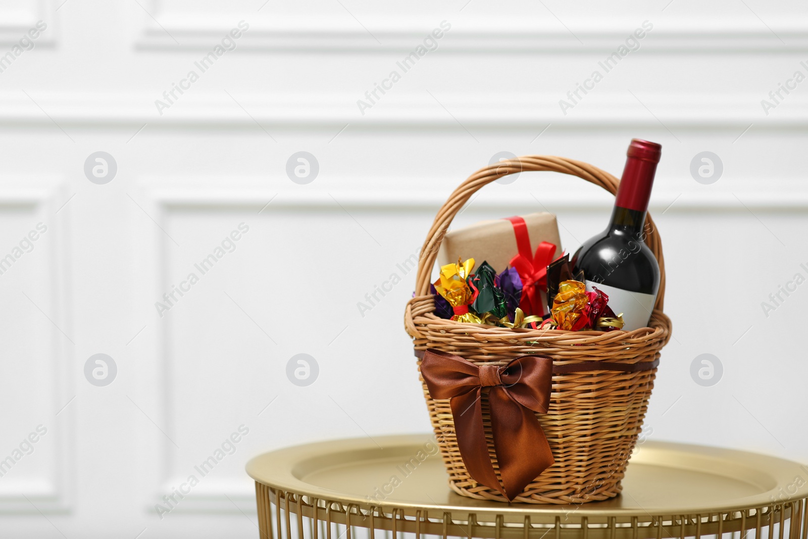 Photo of Gift set in wicker basket on golden table near white wall. Space for text