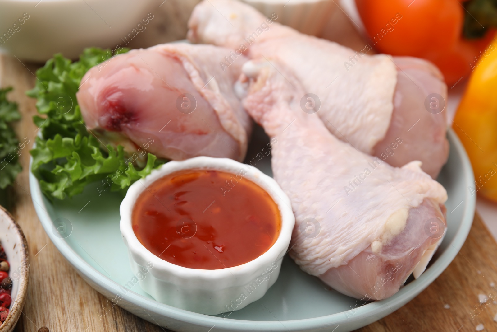 Photo of Fresh marinade, raw chicken drumsticks and lettuce on wooden table, closeup