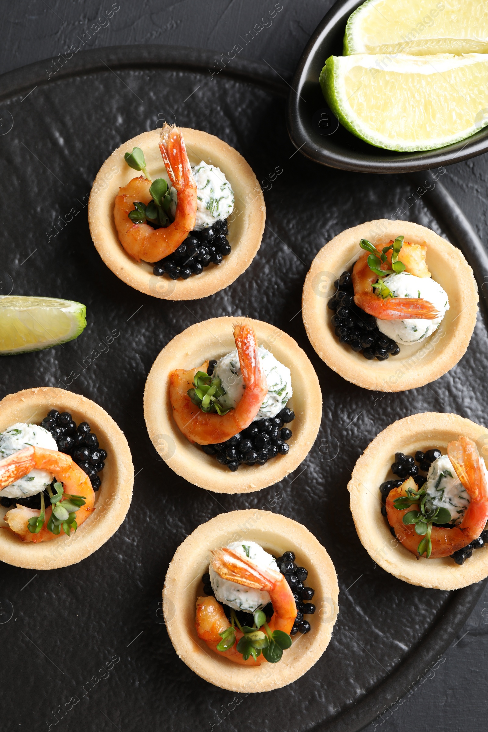 Photo of Delicious canapes with shrimps and black caviar on black textured table, top view