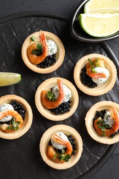 Delicious canapes with shrimps and black caviar on black textured table, top view