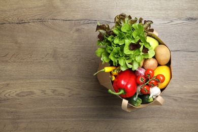 Paper bag full of fresh vegetables on wooden background, top view. Space for text
