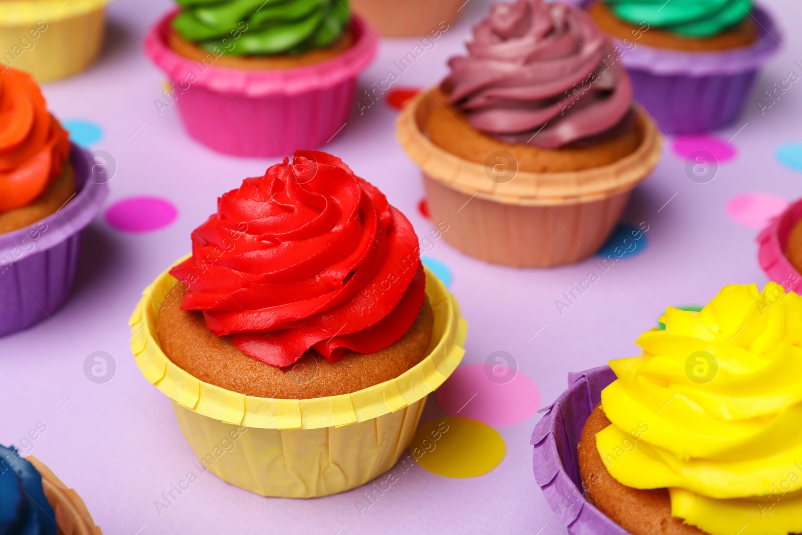 Photo of Many delicious colorful cupcakes and confetti on violet background, closeup