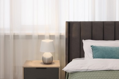 Photo of Comfortable bed with bedding and lamp on wooden bedside table in room