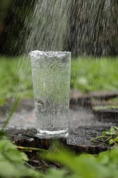 Splashing out water into glass on wooden stump in green grass outdoors