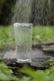 Photo of Splashing out water into glass on wooden stump in green grass outdoors