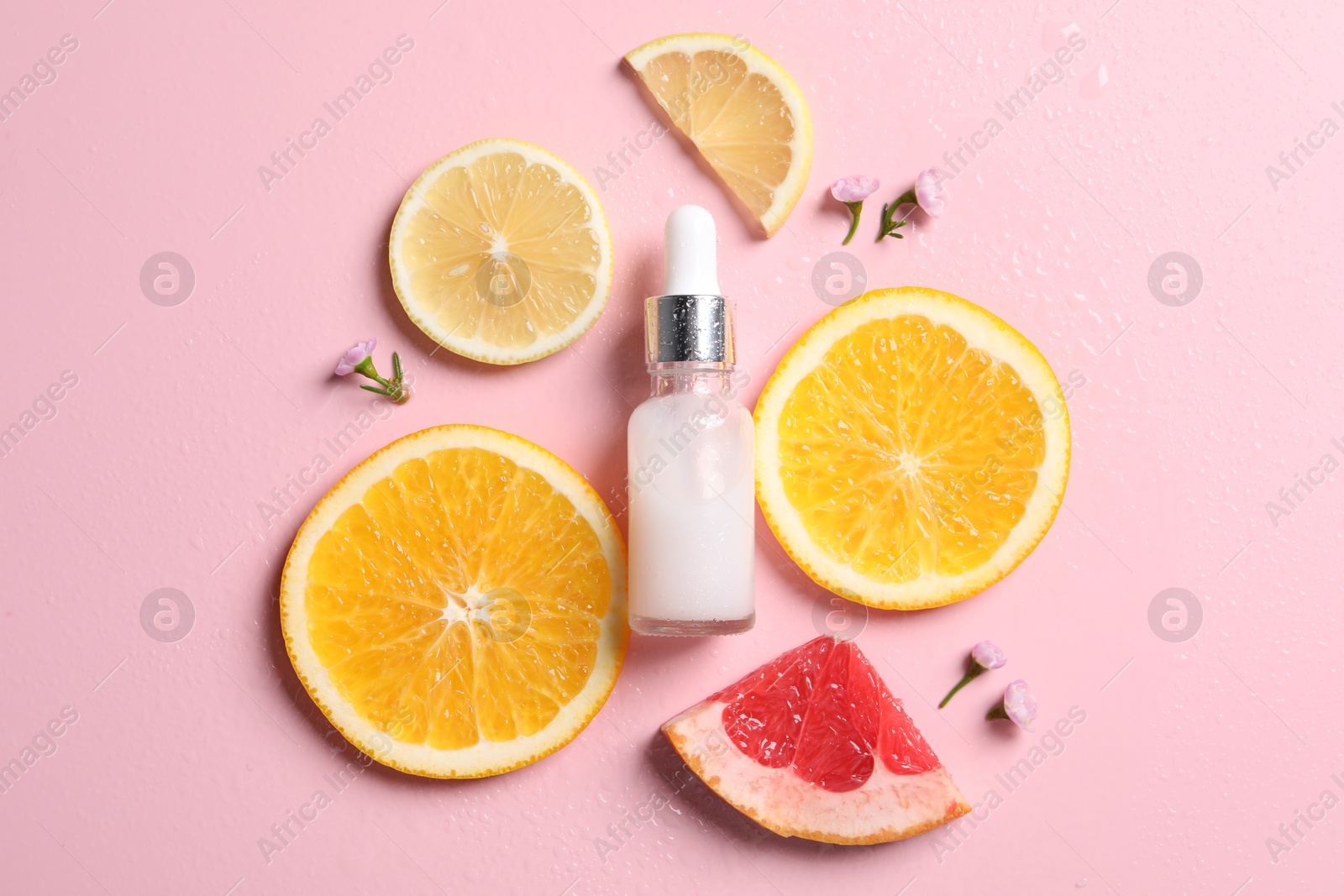 Photo of Bottle of cosmetic serum, sliced citrus fruits and small flowers on wet pink background, flat lay