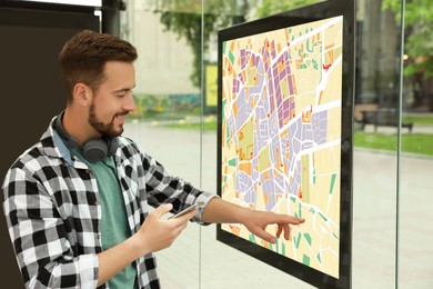 Image of Young man with smartphone near public transport map at bus stop