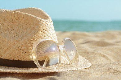 Photo of Hat with beautiful sunglasses on sand near sea, closeup. Space for text