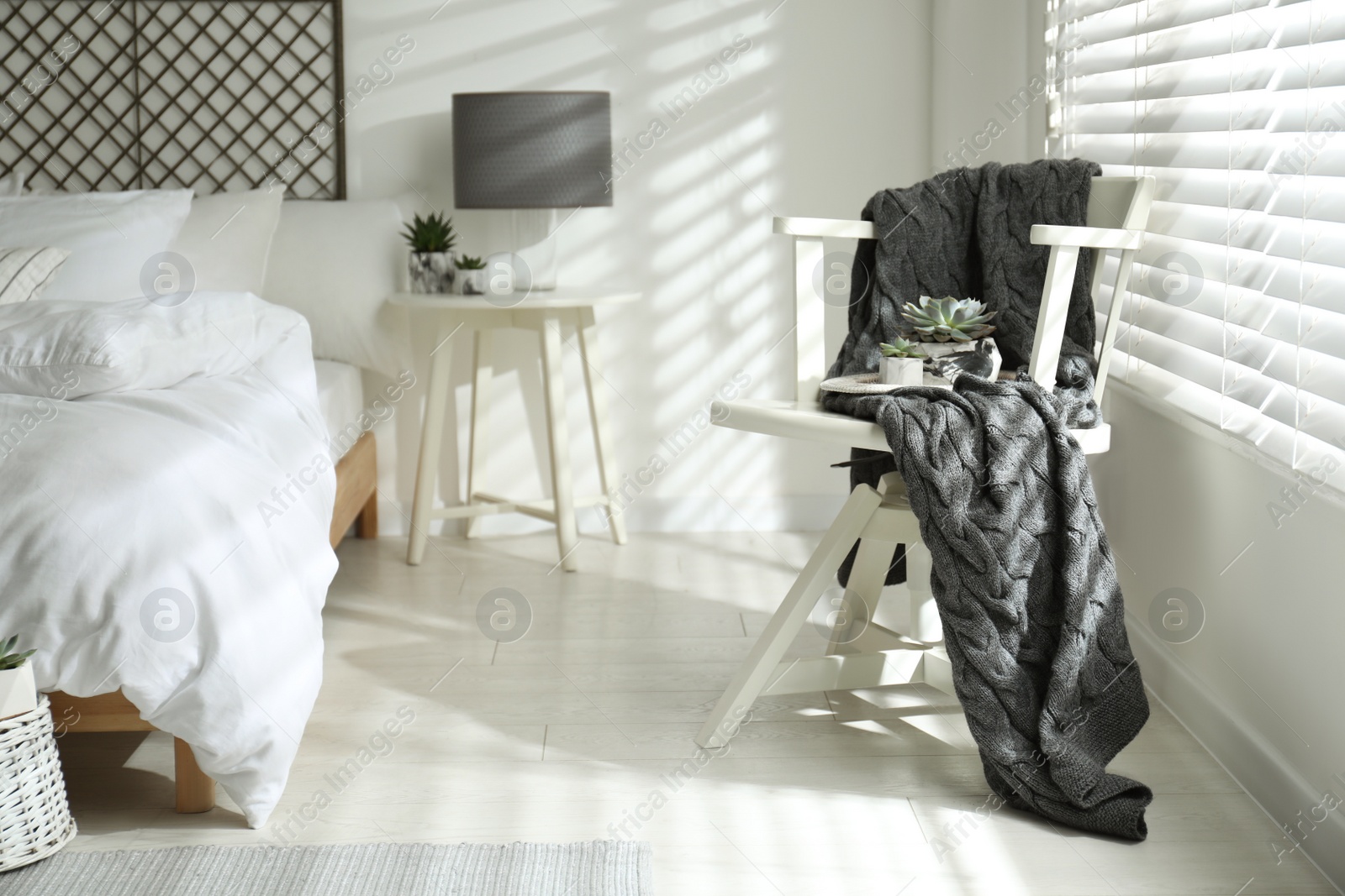 Photo of White chair with warm knitted plaid and succulent plants in stylish bedroom interior