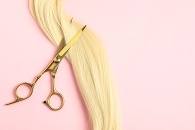 Photo of Professional hairdresser scissors with blonde hair strand on pink background, top view. Space for text