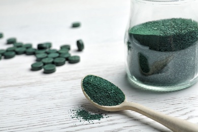 Photo of Spoon and jar of spirulina powder on wooden background. Space for text