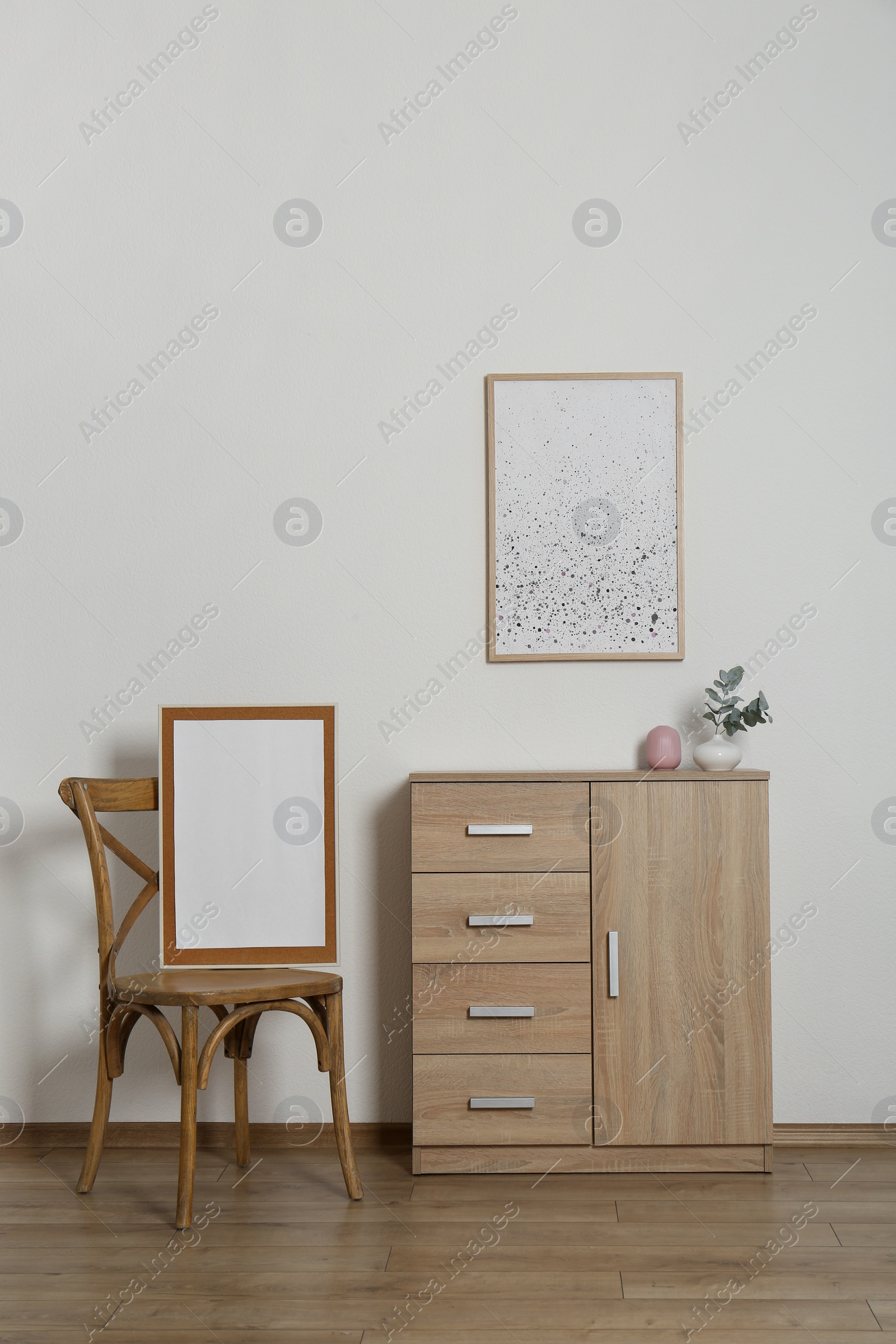 Photo of Wooden chair, chest of drawers, vases and frames in room with light wall. Interior design