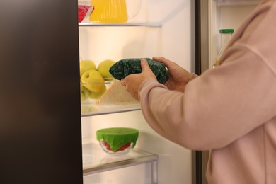 Man putting bowl covered with beeswax food wrap into refrigerator, closeup