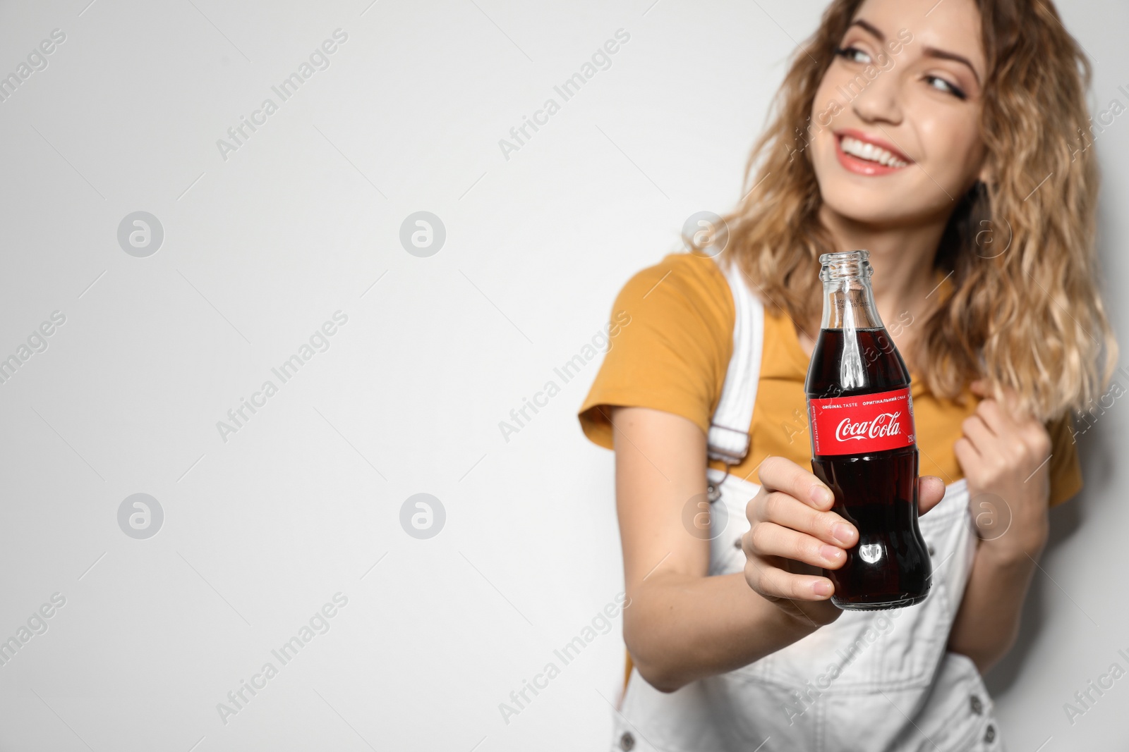 Photo of MYKOLAIV, UKRAINE - NOVEMBER 28, 2018: Young woman with bottle of Coca-Cola on white background, space for text