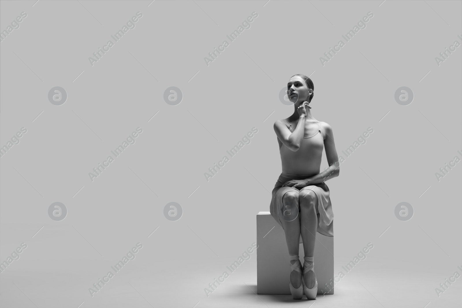 Photo of Young ballerina practicing dance moves on cube, space for text. Black and white effect