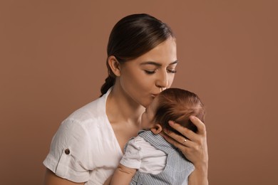 Photo of Mother kissing her cute newborn baby on brown background