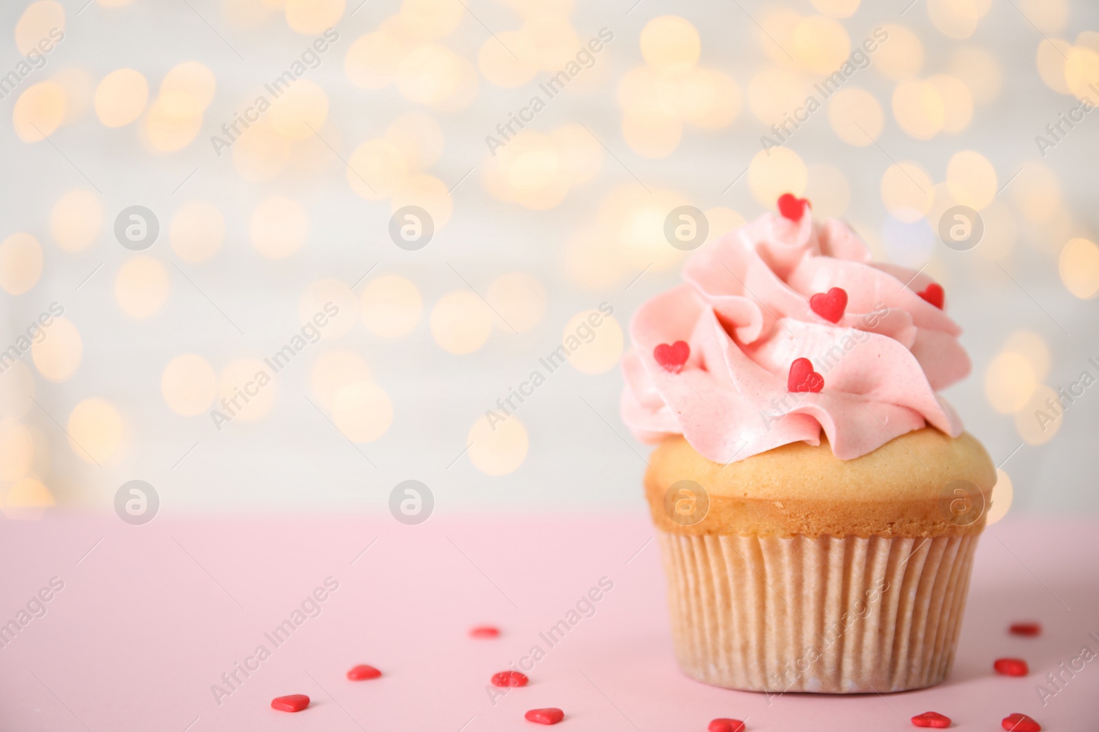 Photo of Tasty cupcake on pink table against blurred lights, space for text. Valentine's Day celebration