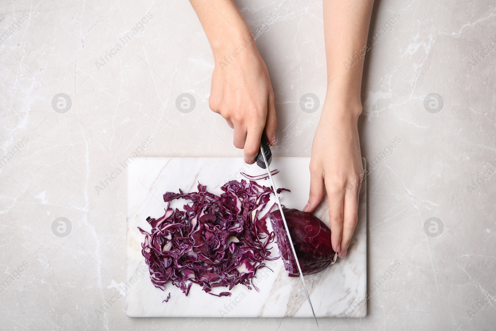 Photo of Woman cutting red cabbage on marble board, top view