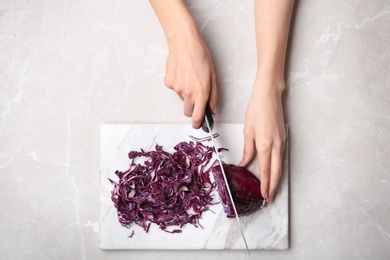 Photo of Woman cutting red cabbage on marble board, top view