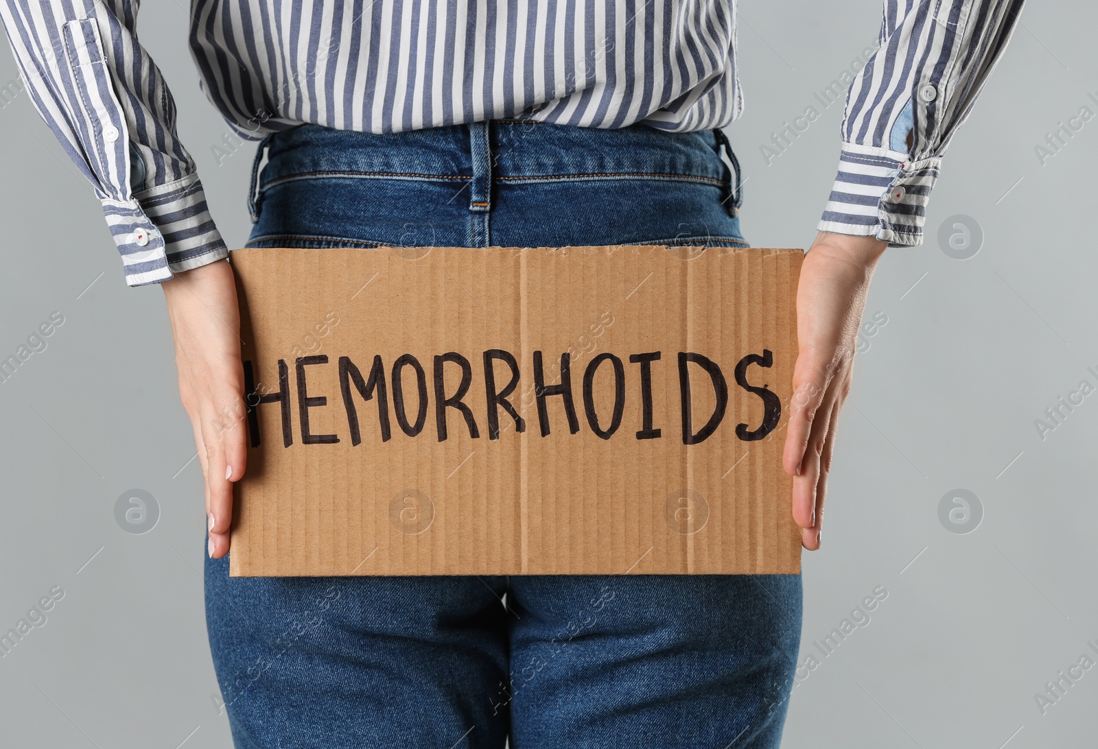 Photo of Woman holding carton sign with word HEMORRHOIDS on light grey background, closeup