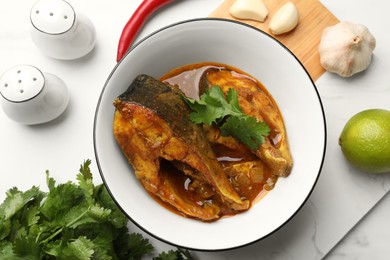 Photo of Tasty fish curry and ingredients on white table, flat lay. Indian cuisine