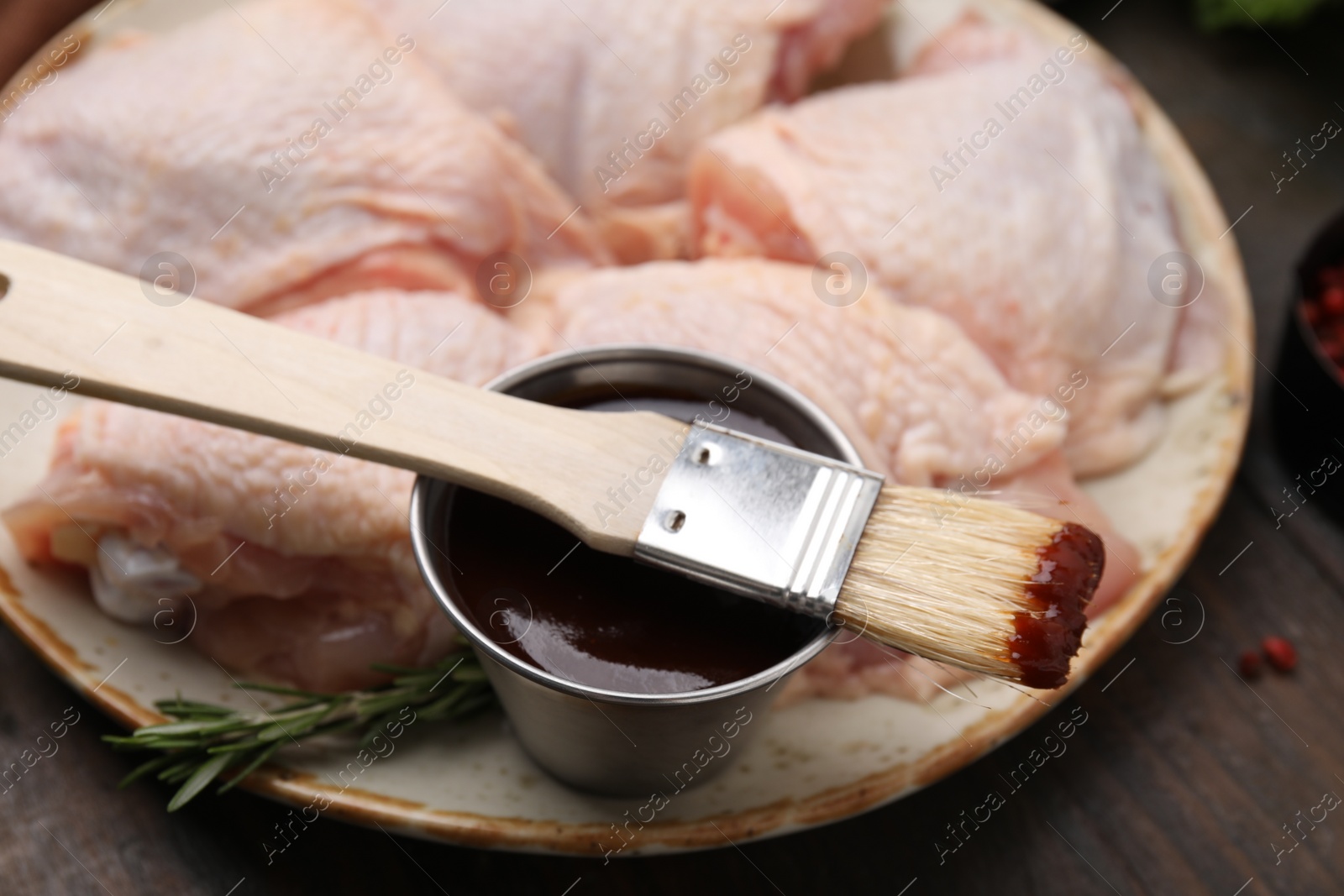 Photo of Plate with fresh marinade, raw chicken and basting brush on wooden table, closeup