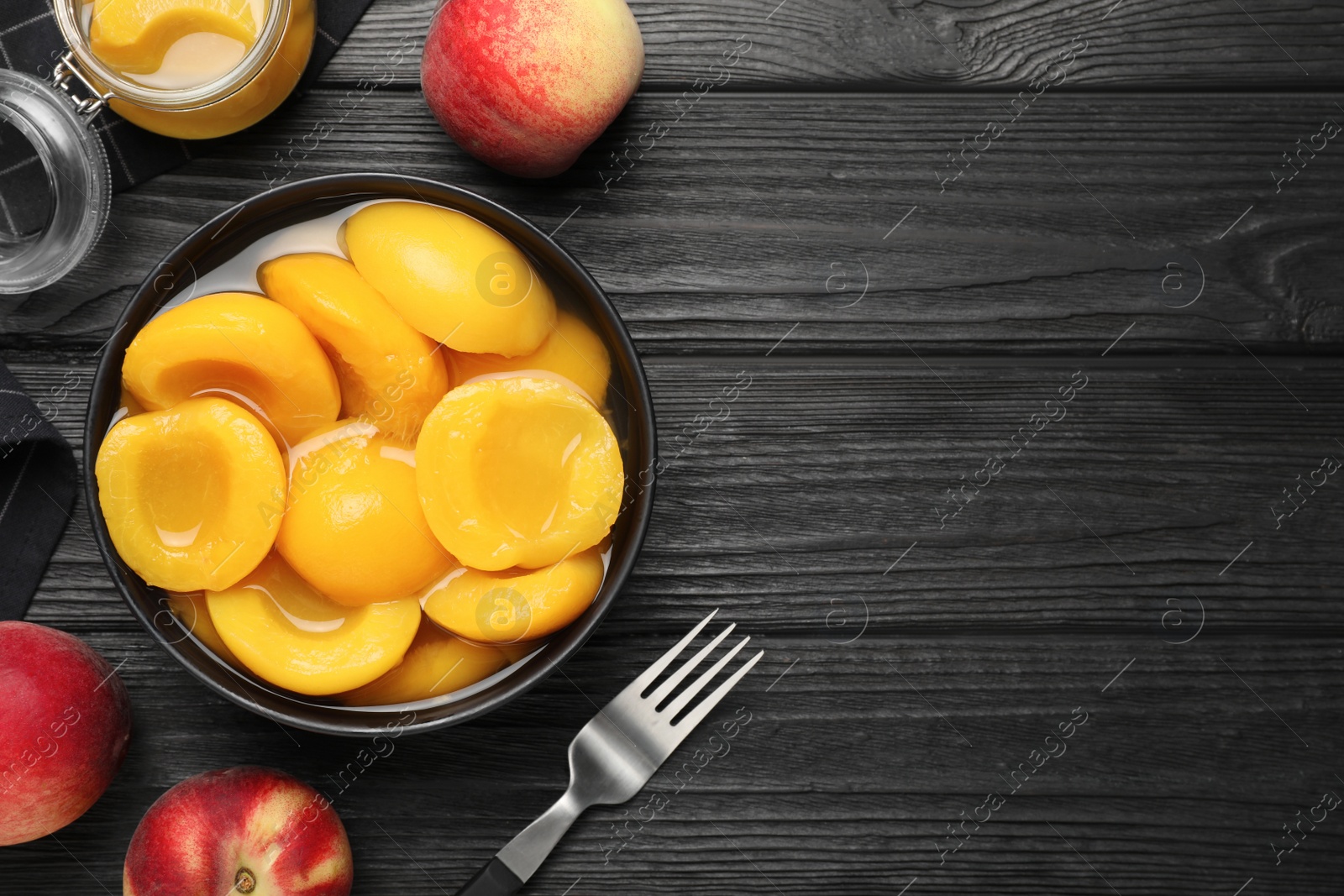 Photo of Canned peach halves on black wooden table, flat lay. Space for text