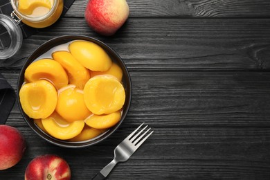 Canned peach halves on black wooden table, flat lay. Space for text