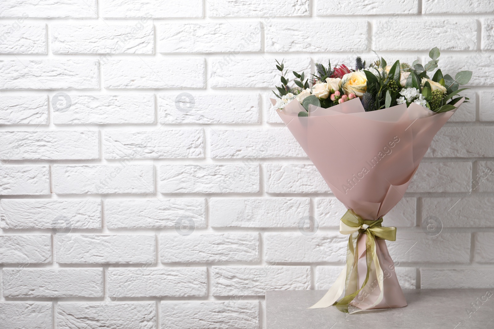 Photo of Beautiful bouquet with roses on light table near white brick wall. Space for text