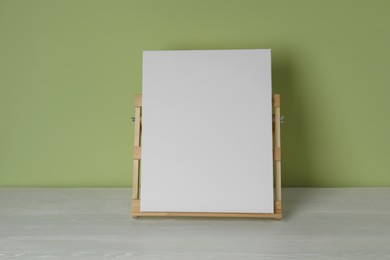 Photo of Wooden easel with blank canvas on white table