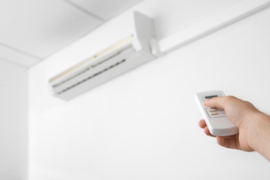 Photo of Man operating air conditioner with remote control indoors