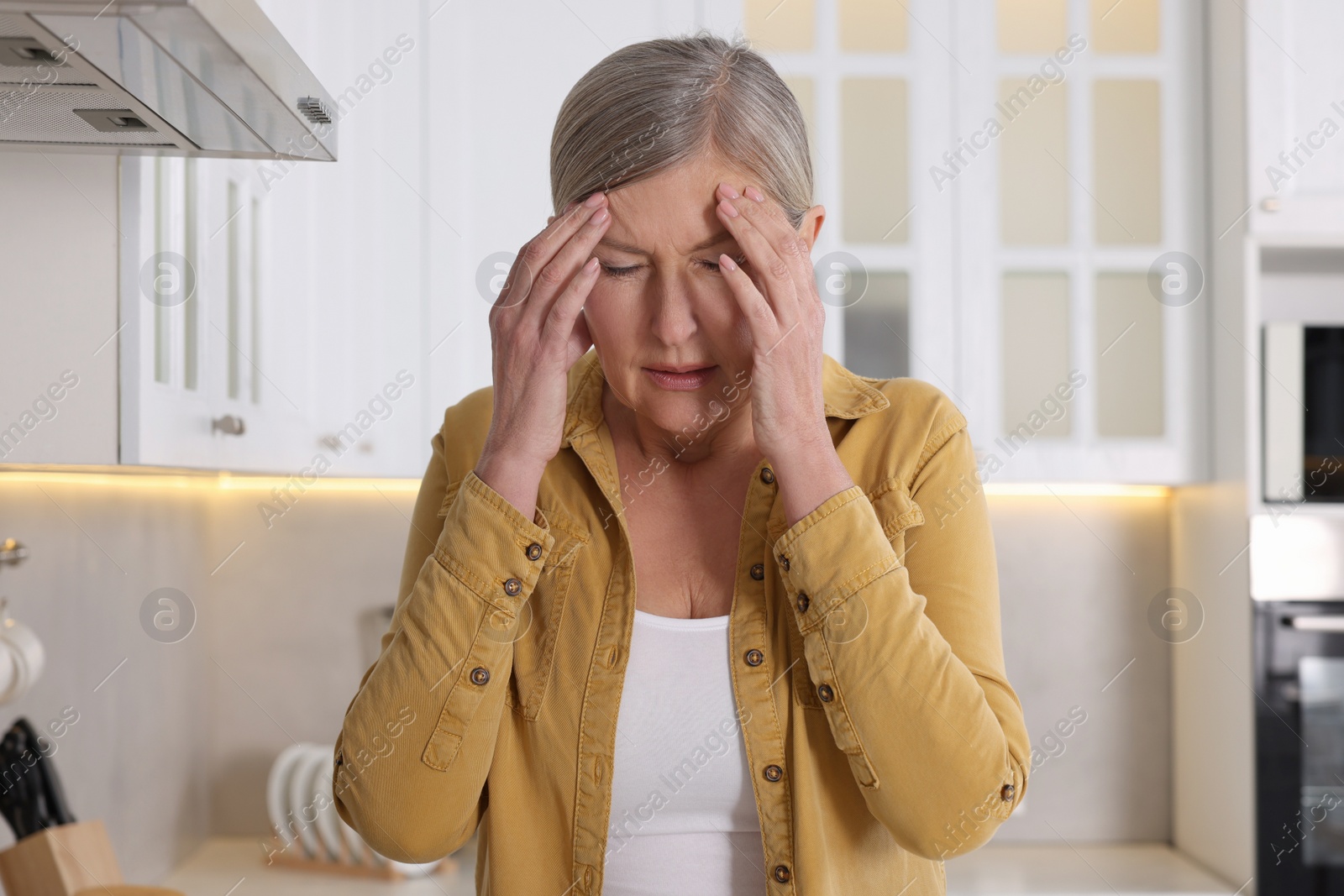 Photo of Menopause. Woman suffering from headache in kitchen