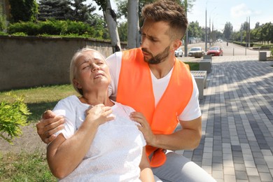 Photo of Worker helping mature woman on city street. Suffering from heat stroke