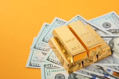 Shiny gold bars and dollar bills on color background