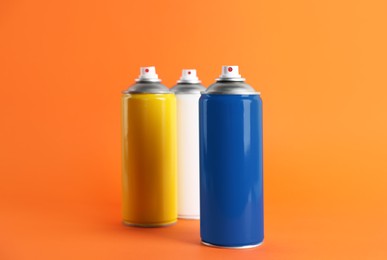 Photo of Colorful cans of spray paints on orange background