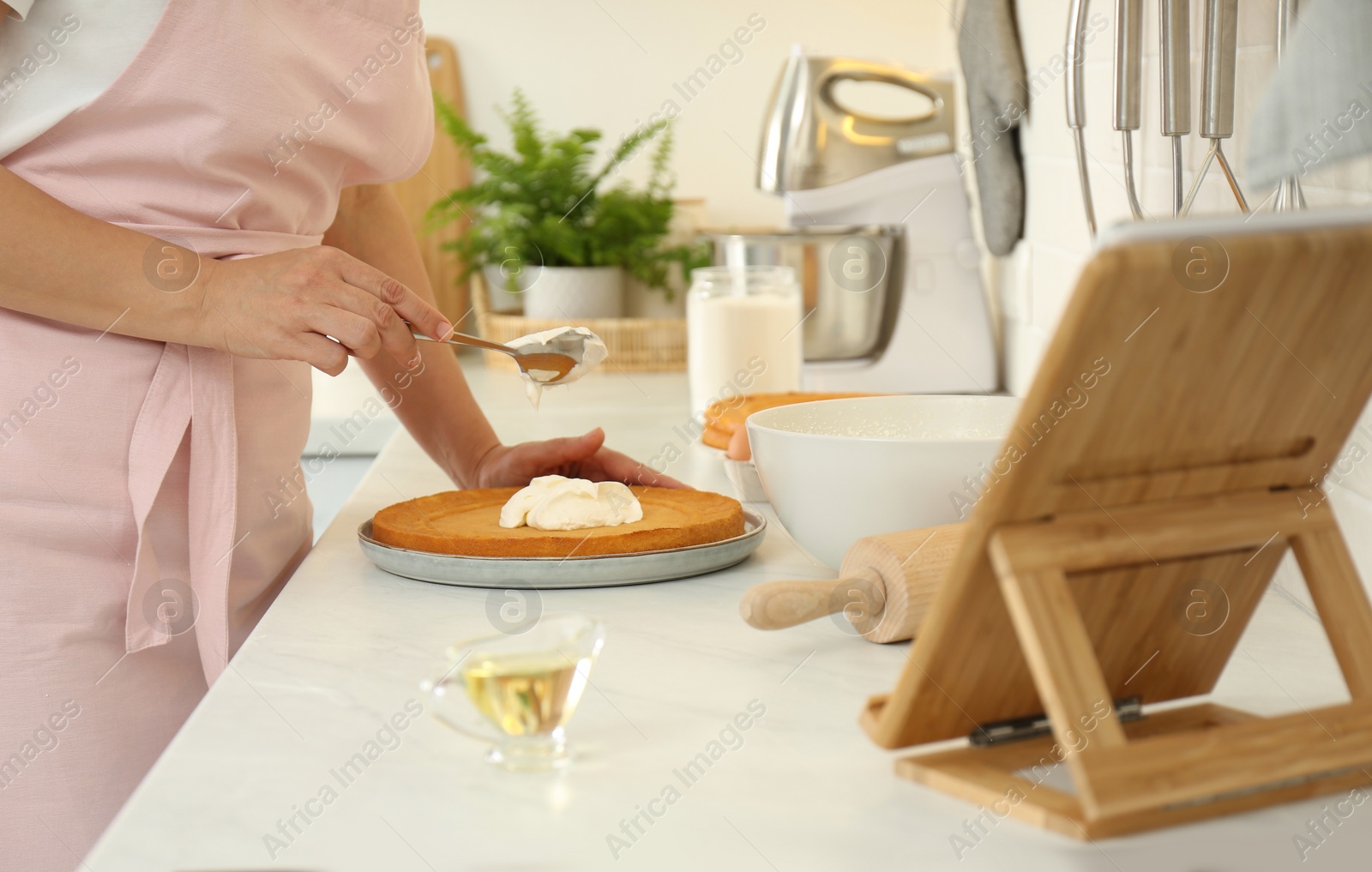 Photo of Woman making cake while watching online cooking course via tablet in kitchen, closeup