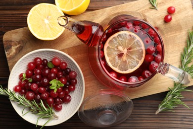 Photo of Tasty hot cranberry tea, lemon, rosemary and fresh berries on wooden table