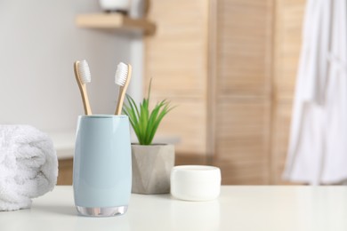 Photo of Bamboo toothbrushes, towel, potted plant and cosmetic product on white countertop in bathroom, space for text