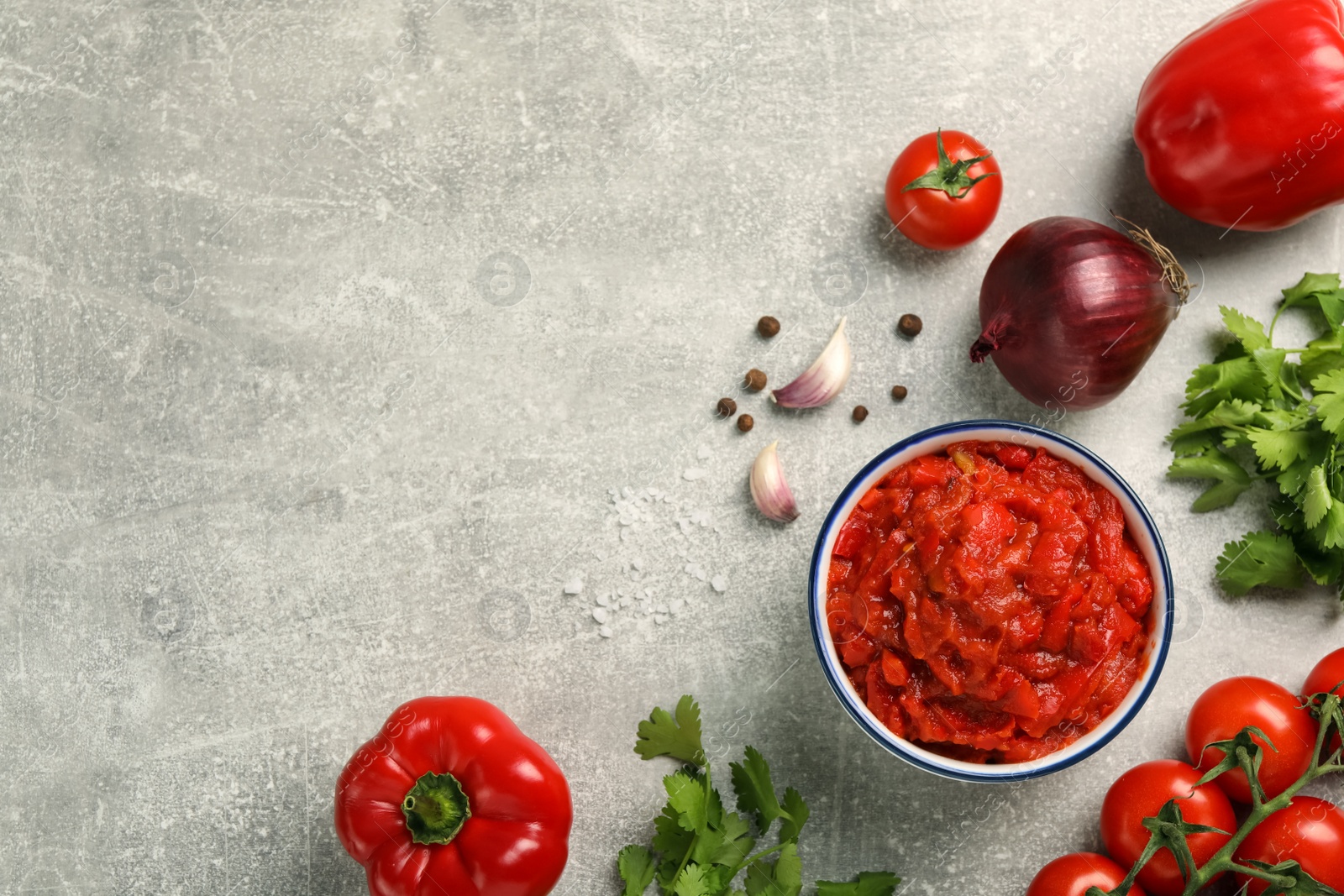 Photo of Delicious lecho in bowl and fresh ingredients on light grey table, flat lay. Space for text