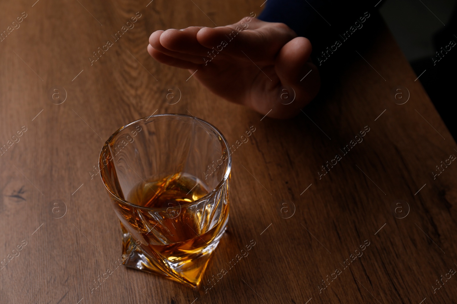 Photo of Man refusing to drink whiskey at wooden table, closeup. Alcohol addiction treatment