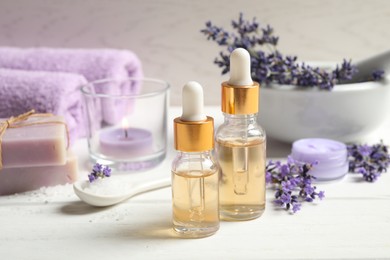 Composition with bottles of essential oil and lavender flowers on white wooden table