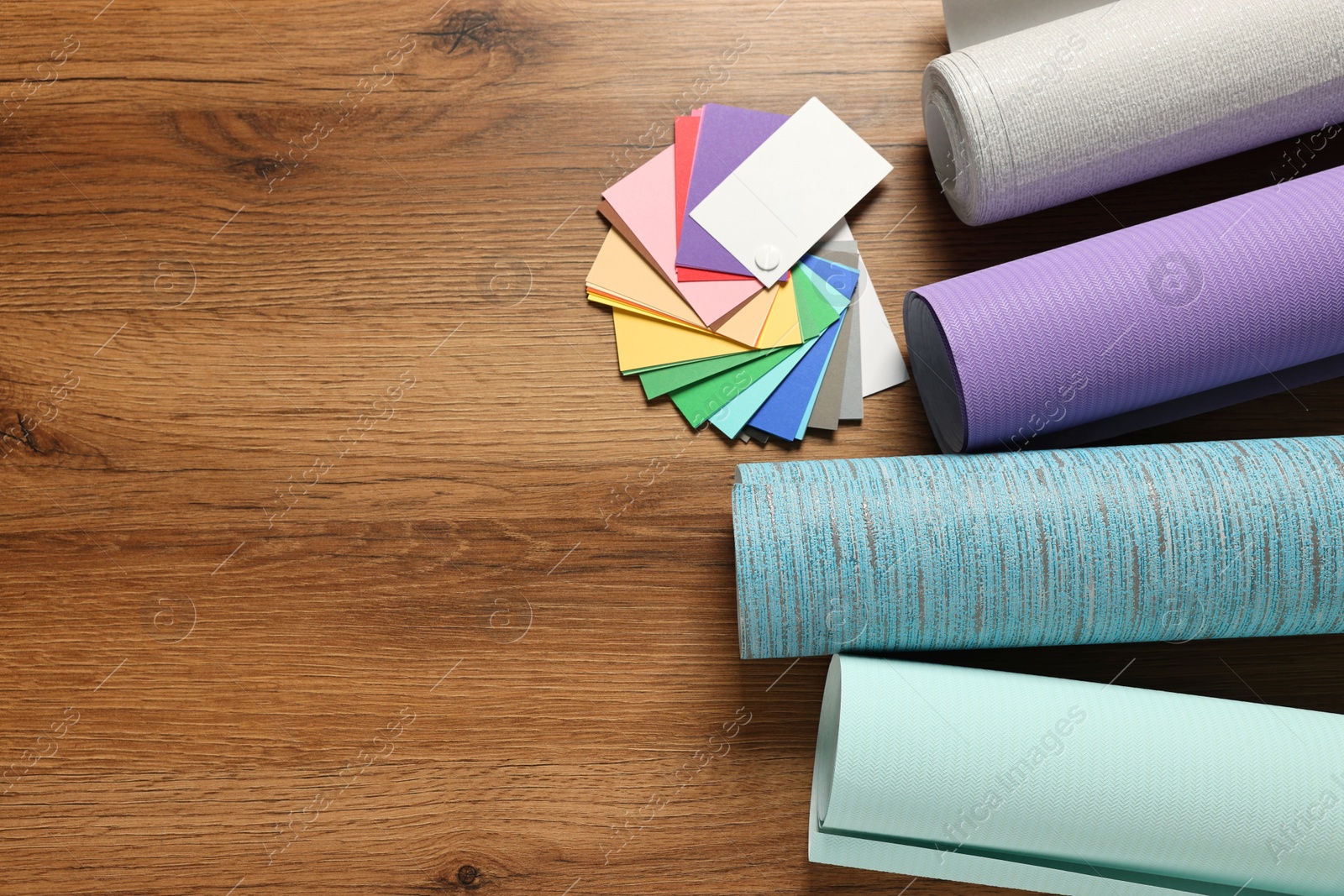 Photo of Different wallpaper rolls and color palette samples on wooden table, flat lay. Space for text